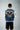 Person wearing a blue jacket with an eagle design and text on the back, standing against a gray background