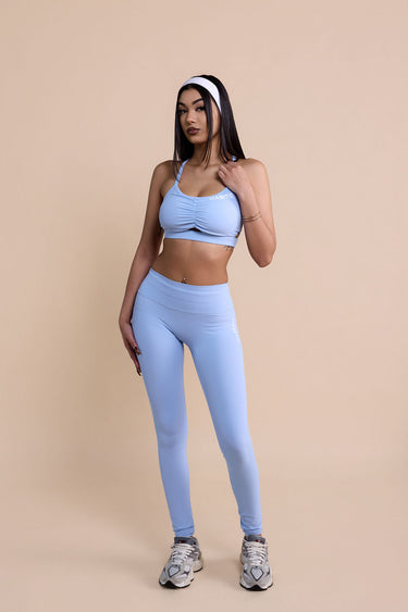 Woman wearing a light blue sports bra and leggings set on a beige background