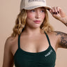 Woman wearing a green sports bra and beige cap with text on a beige background