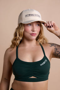 Woman wearing a green sports bra and beige cap with text on a beige background
