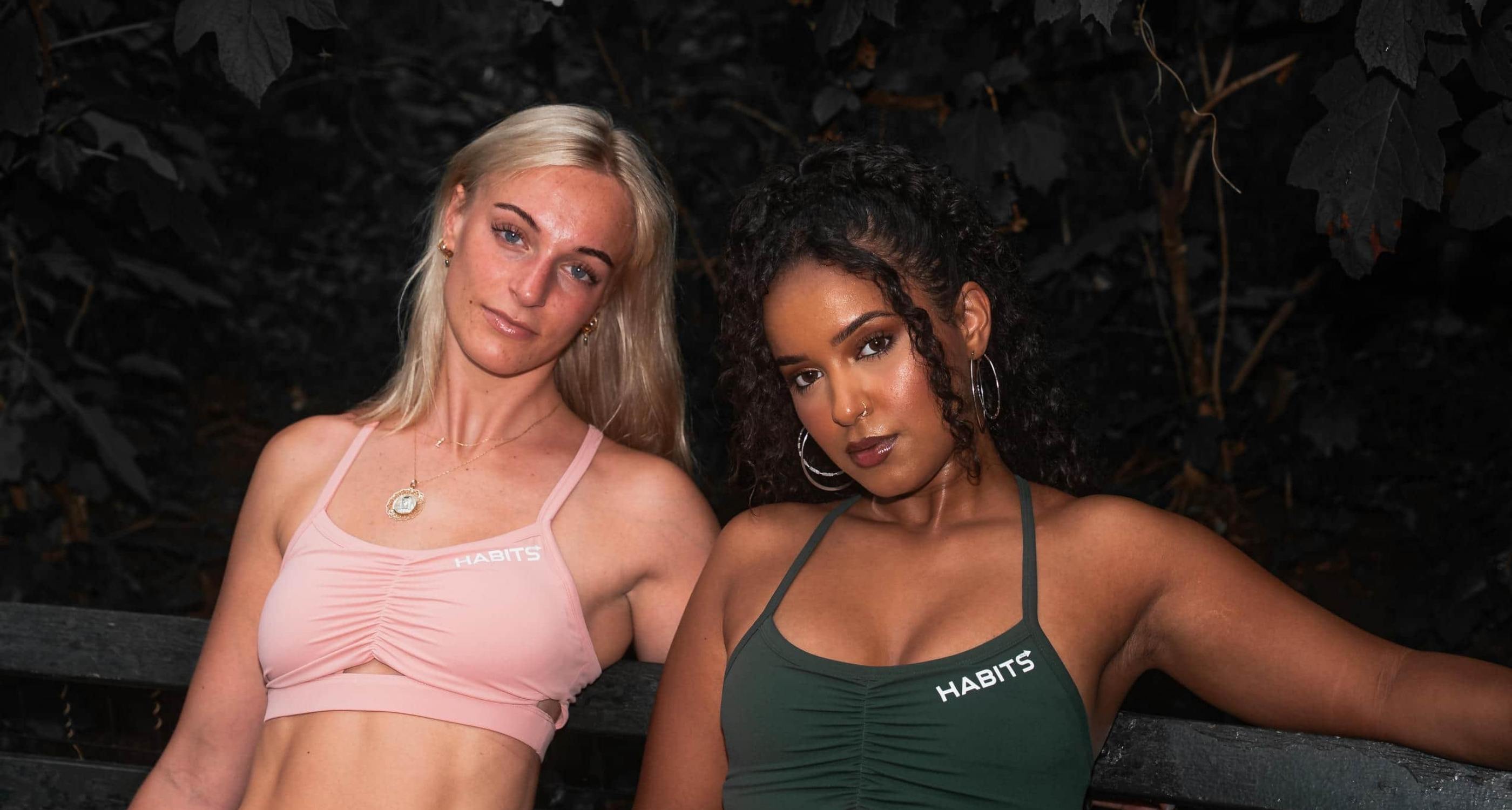 Two women in Habits Sports Bra sitting outdoors with a dark background